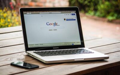 Laptop ouvert sur Google, smartphone à gauche, table en bois, arrière-plan flou